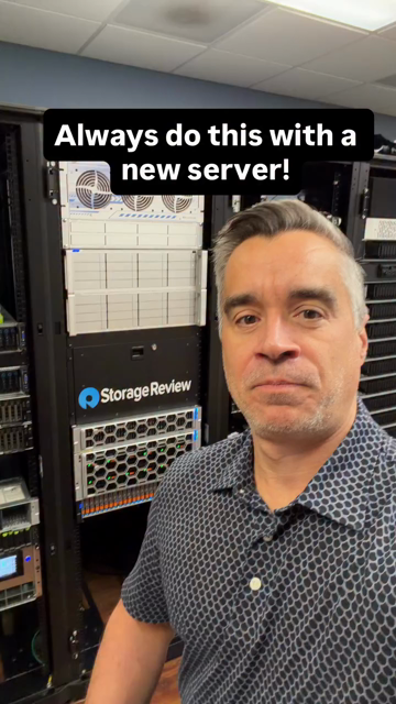 A man with grey hair and a patterned shirt stands in front of a server rack. The rack includes a server from "Storage Review." He points to different parts of the server and talks, but the fan noise is so absolutely fucking deafening that you cant hear anything